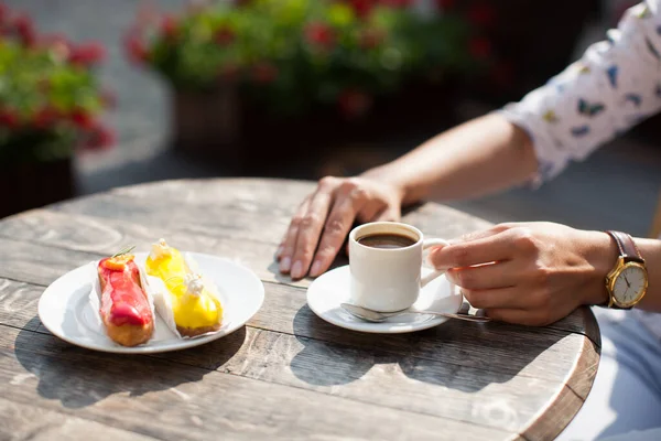 a mug of coffee in hand on table and a delicious eclair on a plate