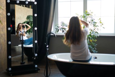 girl photographer with a camera smiling while sitting in the bathroom and looking in the mirror