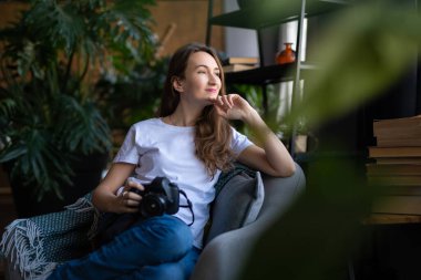 a girl photographer with a camera smiles while sitting in a chair with many books