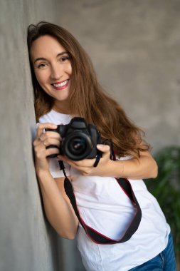 girl photographer with a camera smiling near the wall