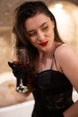 beautiful girl in erotic lingerie sitting in the bathroom with a glass of wine