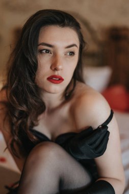 beautiful girl in erotic lingerie sits on a bed in a bedroom decorated with hearts and rose petals