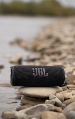 LVIV, UKRAINE - OCTOBER 12, 2022: JBL Flip 6 Black, portable bluetooth speaker outdoors on the stones on the river bank