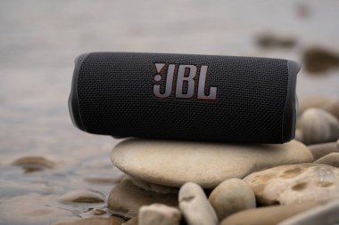 LVIV, UKRAINE - OCTOBER 12, 2022: JBL Flip 6 Black, portable bluetooth speaker outdoors on the stones on the river bank