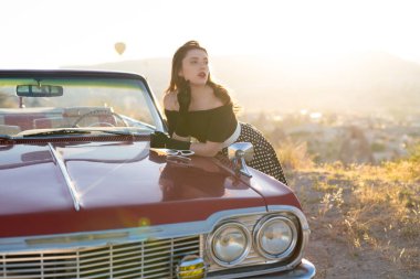 beautiful girl in retro style posing near vintage red cabriolet car