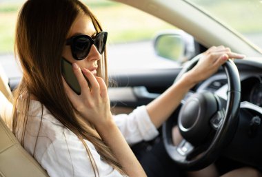 successful business lady driving a car in sunglasses with a mobile phone in her hands