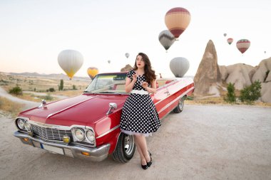 beautiful girl in retro style posing near a vintage red cabriolet car on background of balloons in Cappadocia