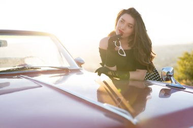 beautiful girl in retro style posing near vintage red cabriolet car