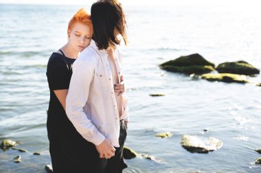 İki aşık oğlan ve kız, deniz kenarındaki kumlu sahilde yürümekten ve sarılmaktan mutlular.