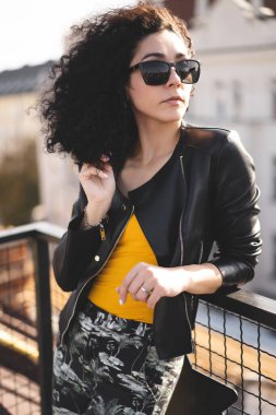 Deri ceketli güzel bir kız şehrin arka planında poz veriyor.