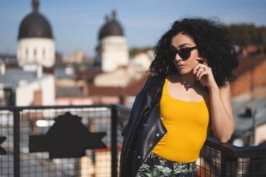 Deri ceketli güzel bir kız şehrin arka planında poz veriyor.