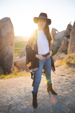 girl hiker in poncho and hat on top of mountain at sunset