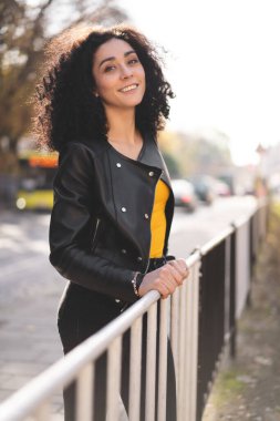 Deri ceketli güzel bir kız şehrin arka planında poz veriyor.