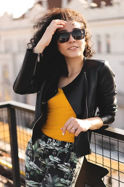 Deri ceketli güzel bir kız şehrin arka planında poz veriyor.