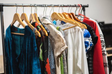 Bir mağazada askılarda birçok farklı renkli kadın kıyafeti var.