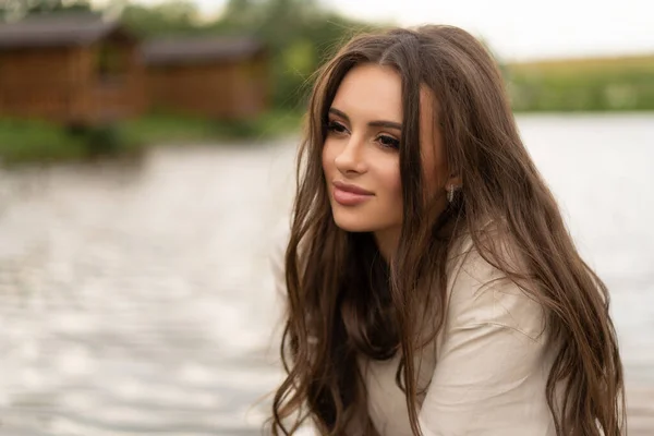 Uzun saçlı güzel bir kız göl kıyısında poz veriyor.