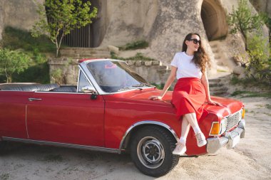 Kapadokya dağlarında eski bir arabanın yanında poz veren etekli güzel mutlu bir kız.