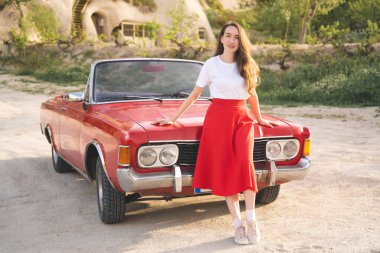 Kapadokya dağlarında eski bir arabanın yanında poz veren etekli güzel mutlu bir kız.