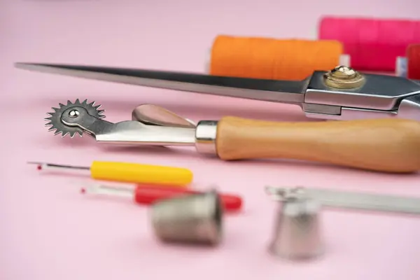 various tailor accessories and tools for tailoring on a pink background