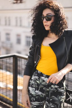 Deri ceketli güzel bir kız şehrin arka planında poz veriyor.