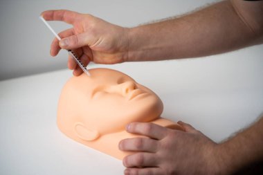 Bir kozmetik uzmanı plastik bir mankenin yüzüne kozmetik şırınga enjekte etmeyi öğrenir.