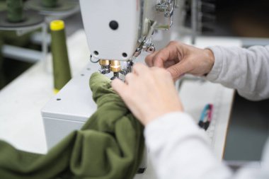 Endüstriyel giysi fabrikasındaki işçiler dikiş makinesine kıyafet dikiyorlar.