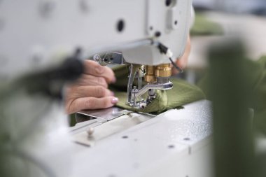 Endüstriyel giysi fabrikasındaki işçiler dikiş makinesine kıyafet dikiyorlar.