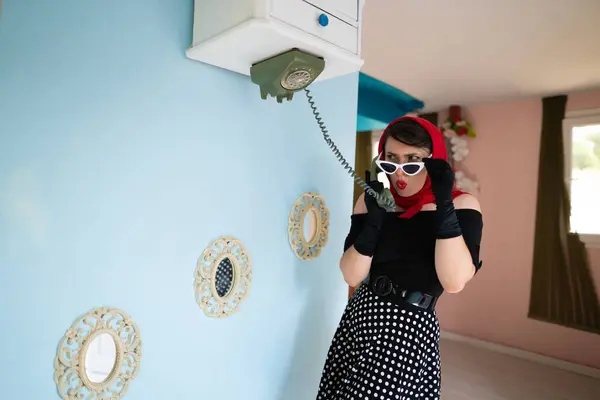 Bir kız ters dönmüş bir evde telefonla konuşuyor, ve mobilyaları da yukarı kaldırıyor.