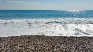 Sahilin güzel manzarası ve mavi gökyüzünün arka planında deniz dalgaları.