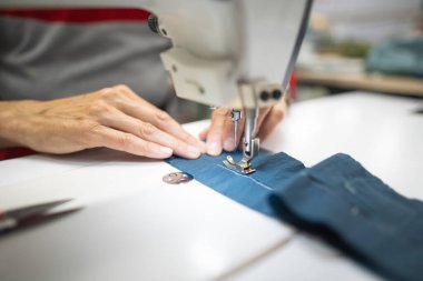 Endüstriyel giysi fabrikasındaki işçiler dikiş makinesine kıyafet dikiyorlar.