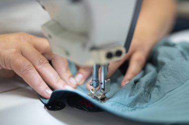 Endüstriyel giysi fabrikasındaki işçiler dikiş makinesine kıyafet dikiyorlar.