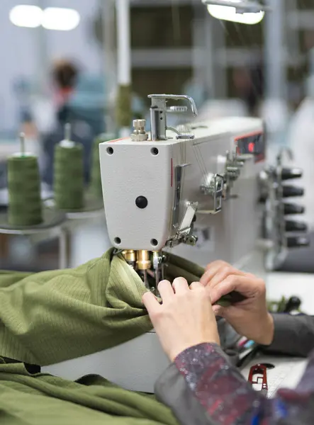 Endüstriyel giysi fabrikasındaki işçiler dikiş makinesine kıyafet dikiyorlar.