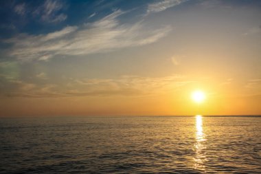 Güzel ve renkli gün batımı, sıcak ışık ve birçok bulut, deniz kıyılarında deniz dalgaları.