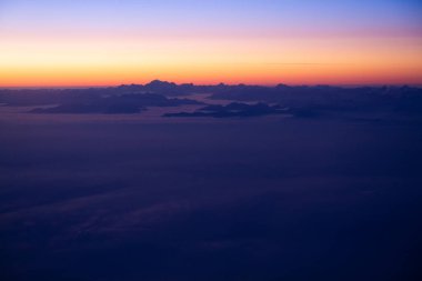 Gökyüzünde güzel, kalın bulutlar uçağın yüksekliğinden gün batımını gören bir manzara.