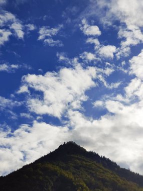 Mavi bulutlu gökyüzünde büyük bir dağın silueti.