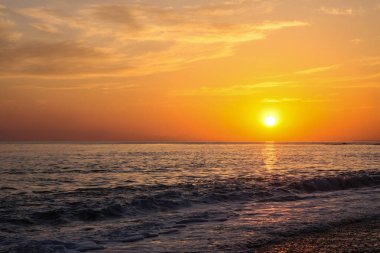 Güzel ve renkli gün batımı, sıcak ışık ve birçok bulut, deniz kıyılarında deniz dalgaları.