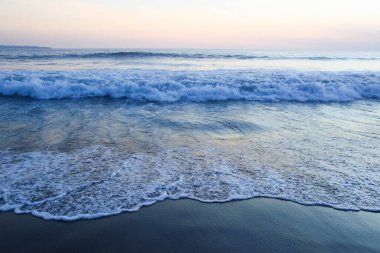 Sahilin güzel manzarası ve mavi gökyüzünün arka planında deniz dalgaları.