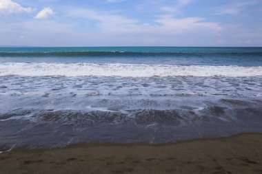 Sahilin güzel manzarası ve mavi gökyüzünün arka planında deniz dalgaları.