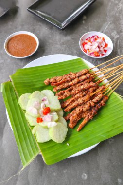 Tavuklu satay ya da satay tavuklu lontong, pirinç keki ve fıstık sosuyla servis edilir. Muz iznine ayrılmış.