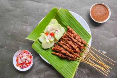 Tavuklu satay ya da satay tavuklu lontong, pirinç keki ve fıstık sosuyla servis edilir. Muz iznine ayrılmış.