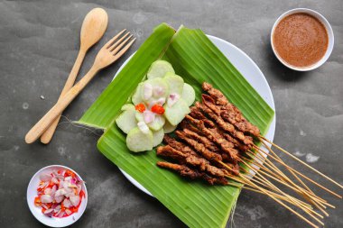 Tavuklu satay ya da satay tavuklu lontong, pirinç keki ve fıstık sosuyla servis edilir. Muz iznine ayrılmış.