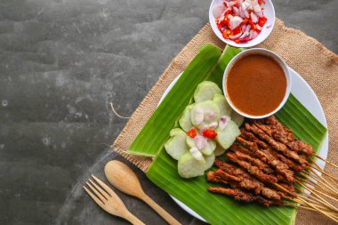 Tavuklu satay ya da satay tavuklu lontong, pirinç keki ve fıstık sosuyla servis edilir. Muz iznine ayrılmış.