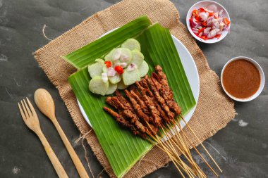 Tavuklu satay ya da satay tavuklu lontong, pirinç keki ve fıstık sosuyla servis edilir. Muz iznine ayrılmış.