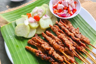 Tavuklu satay ya da satay tavuklu lontong, pirinç keki ve fıstık sosuyla servis edilir. Muz iznine ayrılmış.