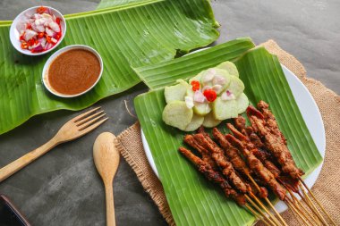Tavuklu satay ya da satay tavuklu lontong, pirinç keki ve fıstık sosuyla servis edilir. Muz iznine ayrılmış.