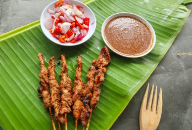 Tavuklu satay ya da satay tavuklu lontong, pirinç keki ve fıstık sosuyla servis edilir. Muz iznine ayrılmış.