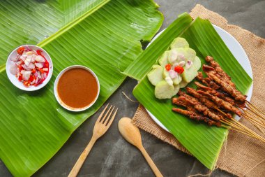 Tavuklu satay ya da satay tavuklu lontong, pirinç keki ve fıstık sosuyla servis edilir. Muz iznine ayrılmış.