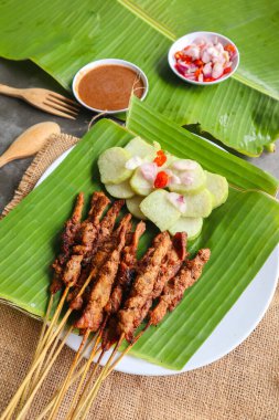 Tavuklu satay ya da satay tavuklu lontong, pirinç keki ve fıstık sosuyla servis edilir. Muz iznine ayrılmış.