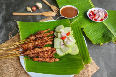 Tavuklu satay ya da satay tavuklu lontong, pirinç keki ve fıstık sosuyla servis edilir. Muz iznine ayrılmış.