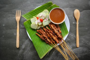 Tavuklu satay ya da satay tavuklu lontong, pirinç keki ve fıstık sosuyla servis edilir. Muz iznine ayrılmış.